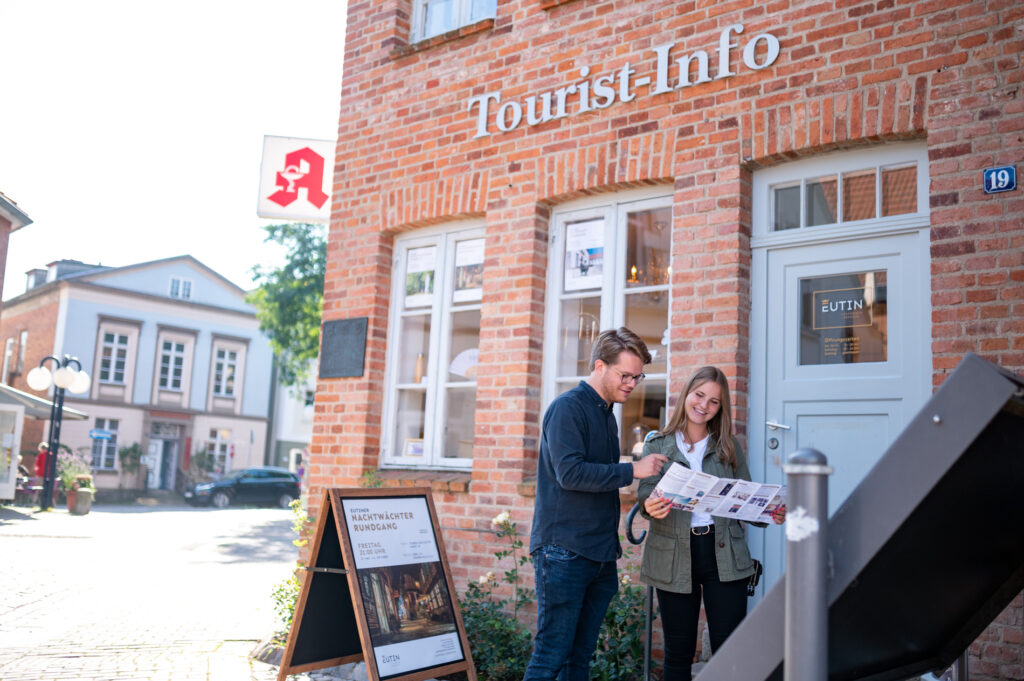 Paar mitte 30 vor der Touristinfo Eutin mit einem Flyer über das Freizeitangebot der Region in der Hand